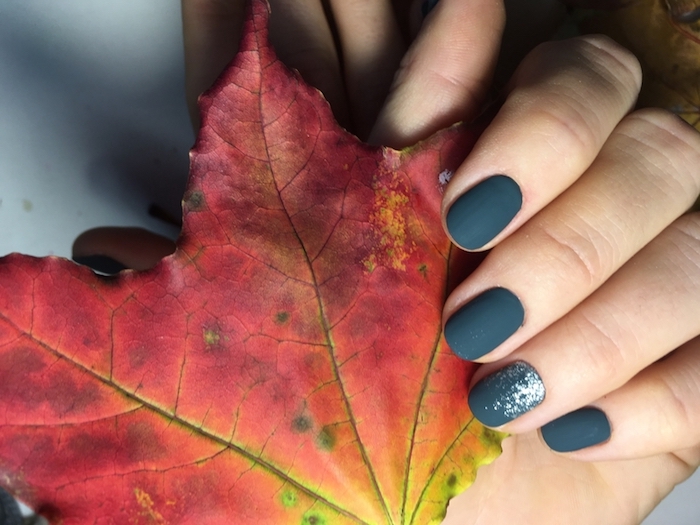 nagellack farben trends herbst eine hand mit dunkelgrünem nagellack und ein herbstblatt eines baumes