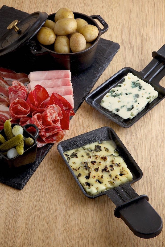 schinken und oliven salami die raclette zutaten zwei kleine schwarze üfännchen mit geschmolzenem käse