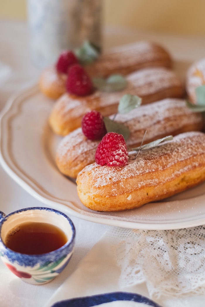 tasse tee eine weiße decke weißer teller mit kleinen churros mit roten himbeeren und grüner pfefferminze