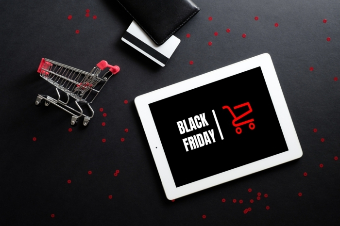 black friday sale concept. tablet with sign "black friday" on screen, shopping cart and debit card over black background. flat lay, top view, overhead.