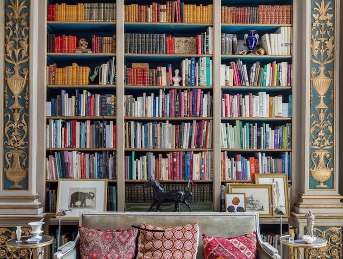 boho style wohnen wohnzimmer große bibliothek aus holz gold blau eingebaut sofa hellgrün rote kissen tisch
