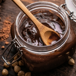 kakaopulver und haselnüsse auf tisch aus holz ein glas mit einer nutella alternative vegan