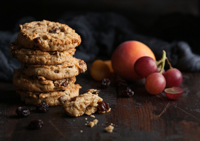 homemade organic oatmeal cookies with raisins and apricots on dark wooden background with apricot and grapes.