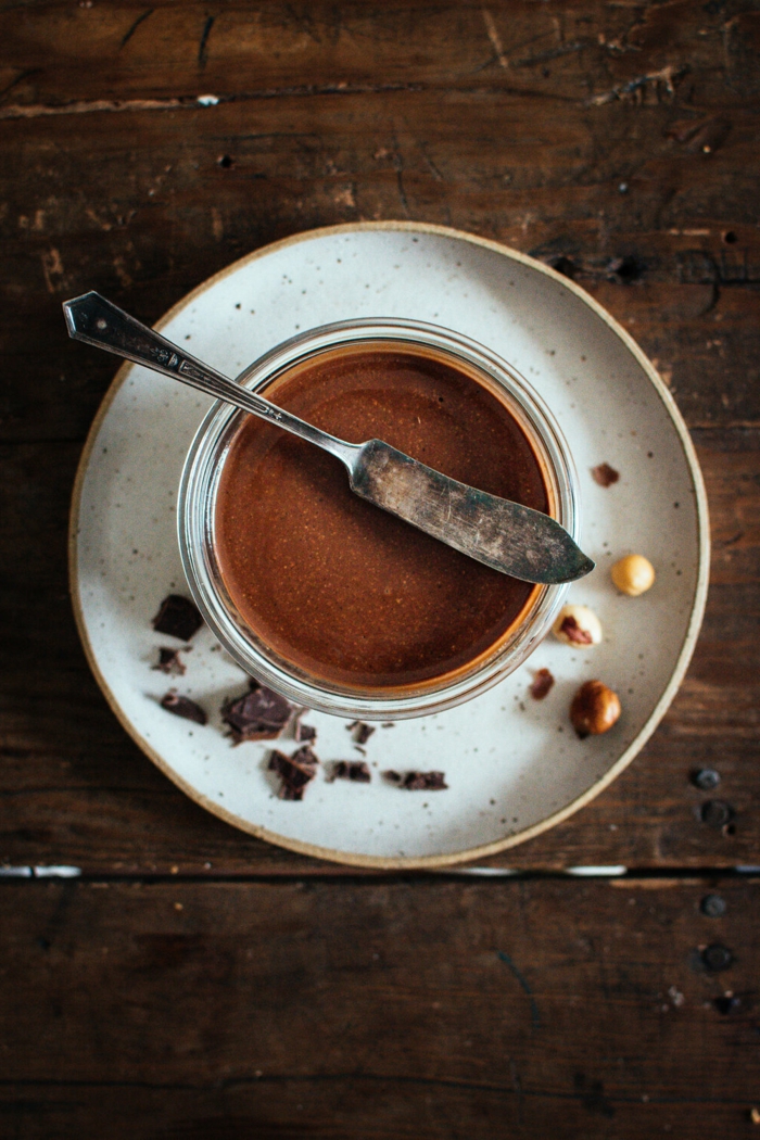 kleiner weiér teller mit haselnüssen ein löffel und glas mit nutella tisch aus holz