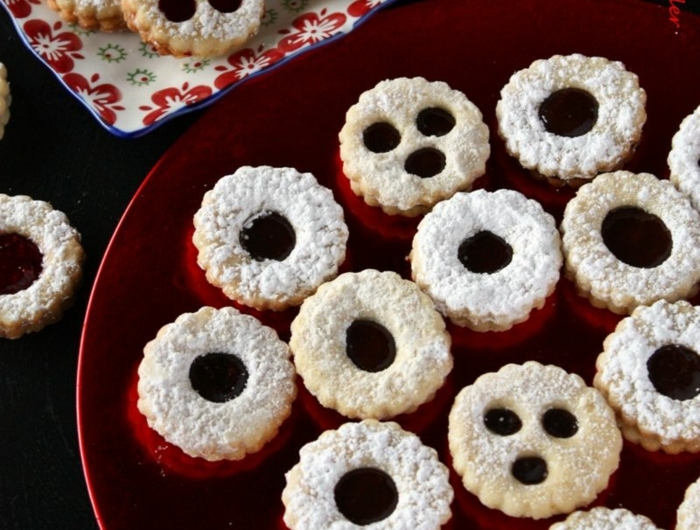 spitzbuben mit mandeln macadamia und kirschenmarmelade roter teller mit weihnachtsplätzchen bestreut mit puderzucker