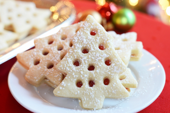 tannenbaum weihnachtsplätzchen mit marmelade spitzbuben kekse weihnachtsgebäck ideen plätzchen auf einem weißen teller tisch mit roter tischdecke bunte weihnachtskugeln