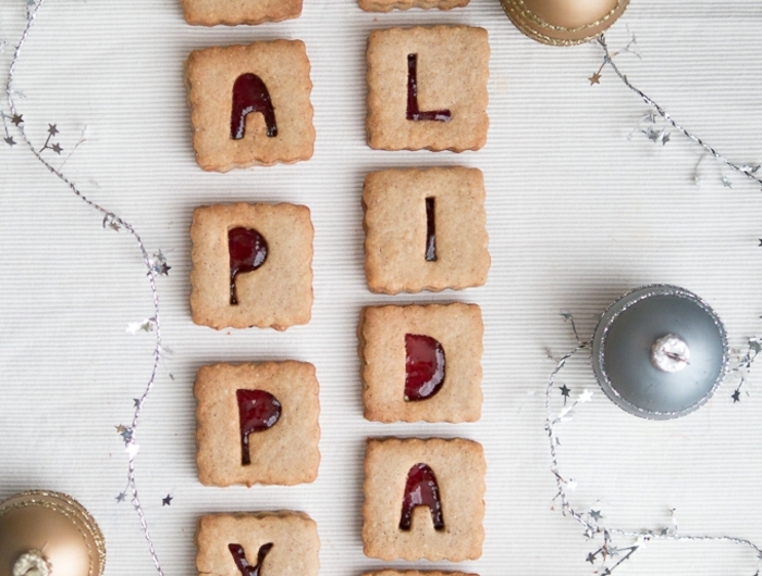 weihnachten kekse plätzchen mit marmelade aus cranberrys happy holidays aufschrift goldene und silberne weihnachtskugeln schöne weihnachtsdekorartion große grün bemalte muschel