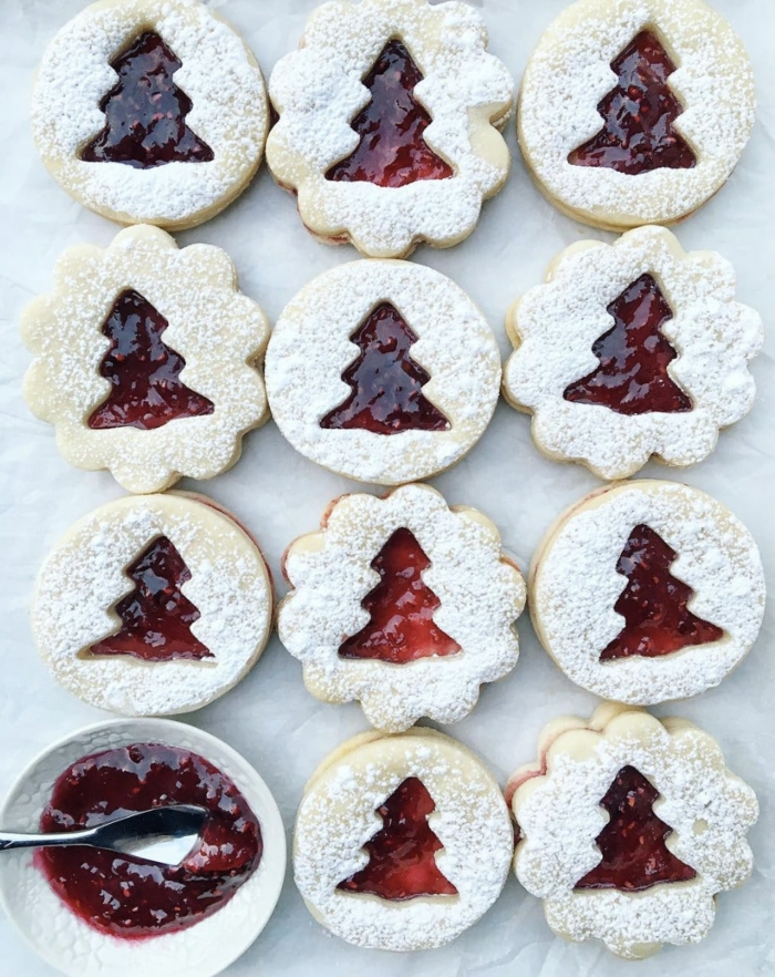 weihnachtsplätzchen mit marmelade mit tannenbaum form auf einem backblech kekse bestreut mit puderzucker