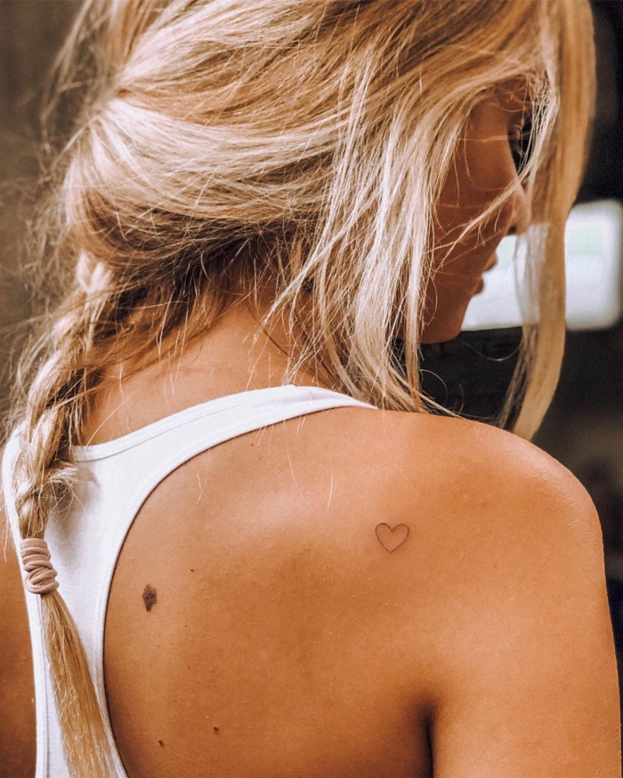 blonde frau lange haare im zopf weißes top originelle tattoo ideen minimalistisch kleines schwarzes herz tätowierung 