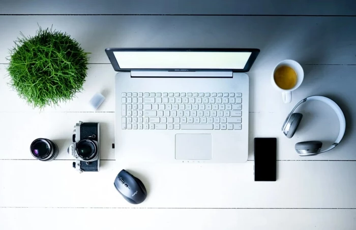 büro einrichten große kopfhörer grüne pflanze tasse mit kaffee fotoaparat schwarzes handy mac book laptop