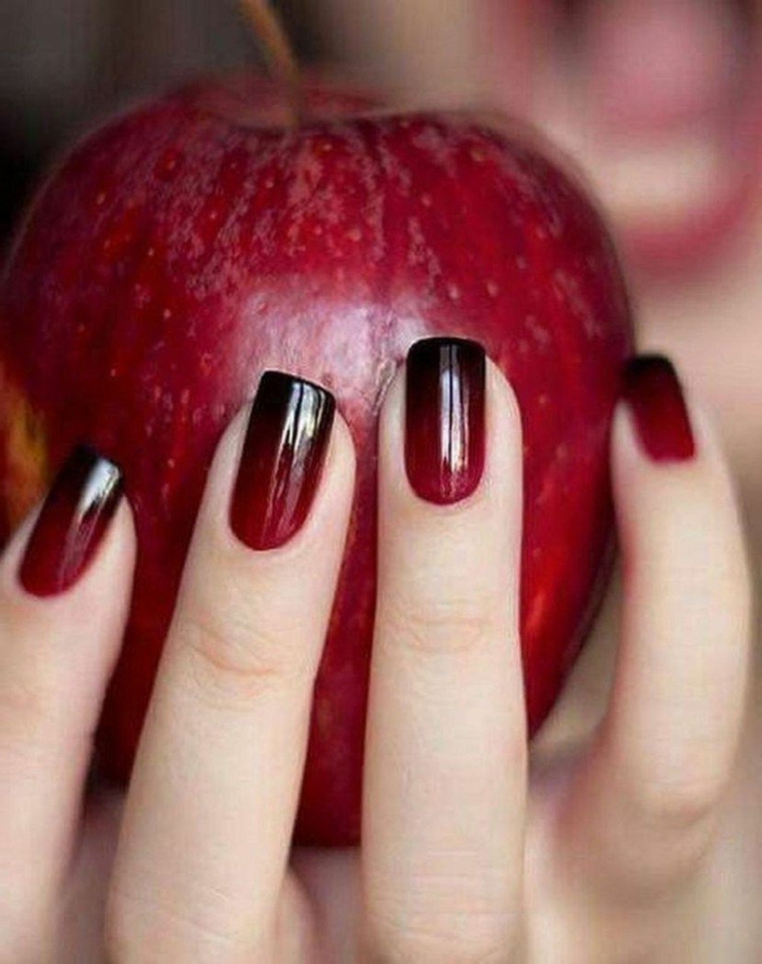 hand hält großen roten apfel schöne gelnägel ombre nägel schwarz rot verlaufend squoval nagelform kürzere nägel maniküre