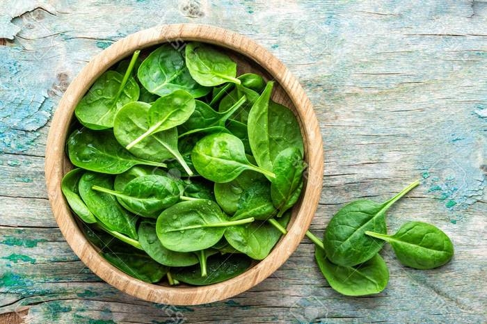 fresh baby spinach leaves in bowl on wooden background