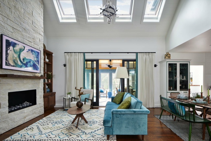 attraktives blaues sofa grüne kissen weiße backsteinwand bunter teppich ovaler kaffeetisch velux austauschfenster abstraktes gemälde