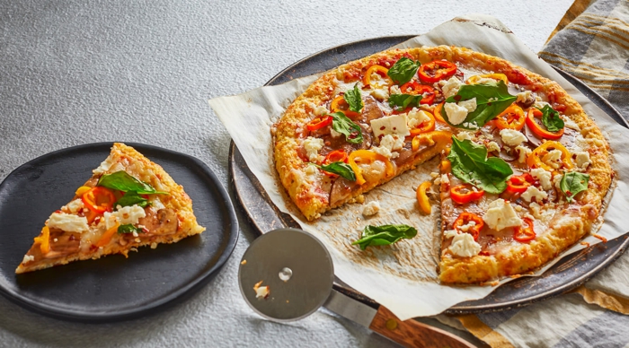 ein grauer teller mit einem stück pizza mit blumenkohl und basilikum und frischen tomaten