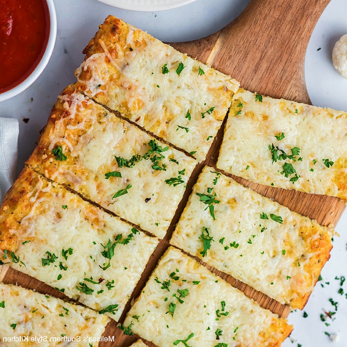 ein holzbrett mit einer pizza mit blumenkohl und mit frischen petersilienblättern