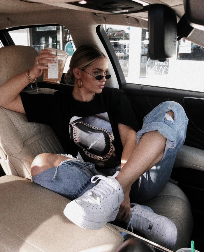 foto im auto moderne weiße sneakers baddie aesthetic casual outfit jeans und schwarzes t shirt hochgesteckte haare mini sonnenbrillen