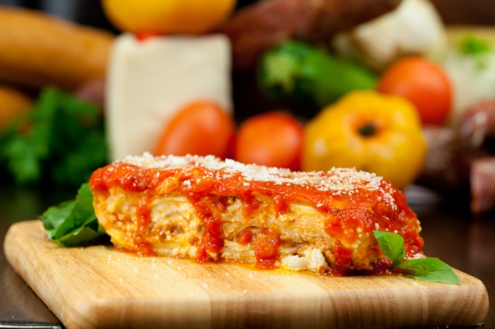 ein brett aus holz und ein stück lasagne mit tomaten sße und parmesan geschmolzenem käse