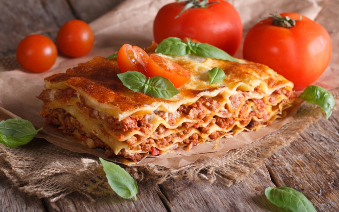 ein tisch aus holz frische tomaten und basilikum blätter eine lasagne mit fascjiertes und käse