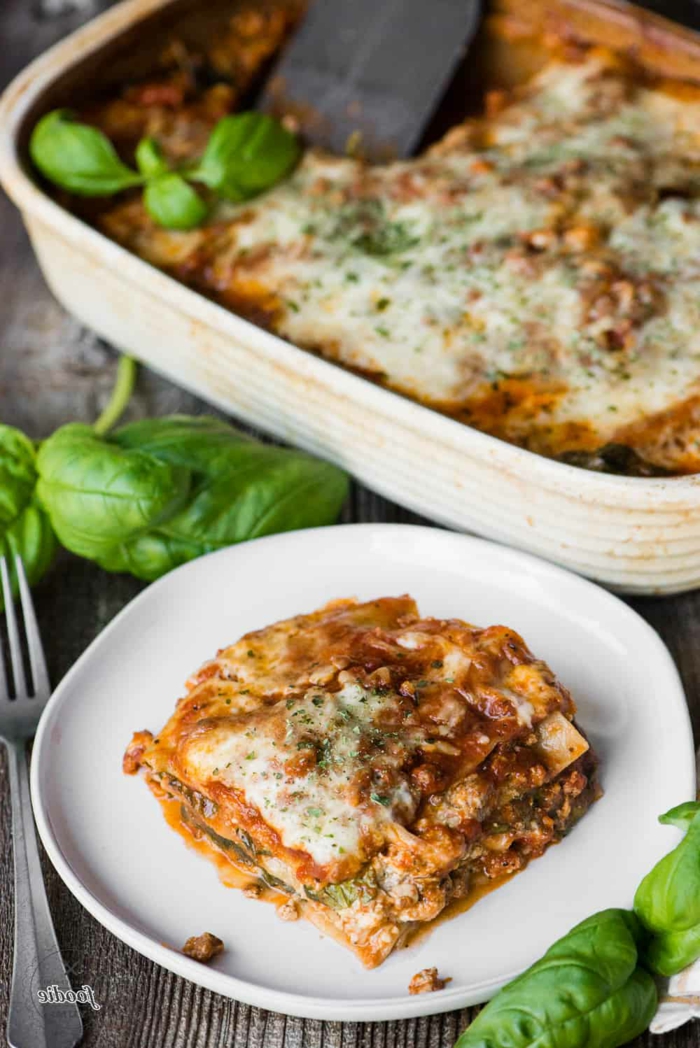 frische basilikum blätter ein weißer teller mit einer lasagne mit spinat lasagne vegetarisch eine gabel