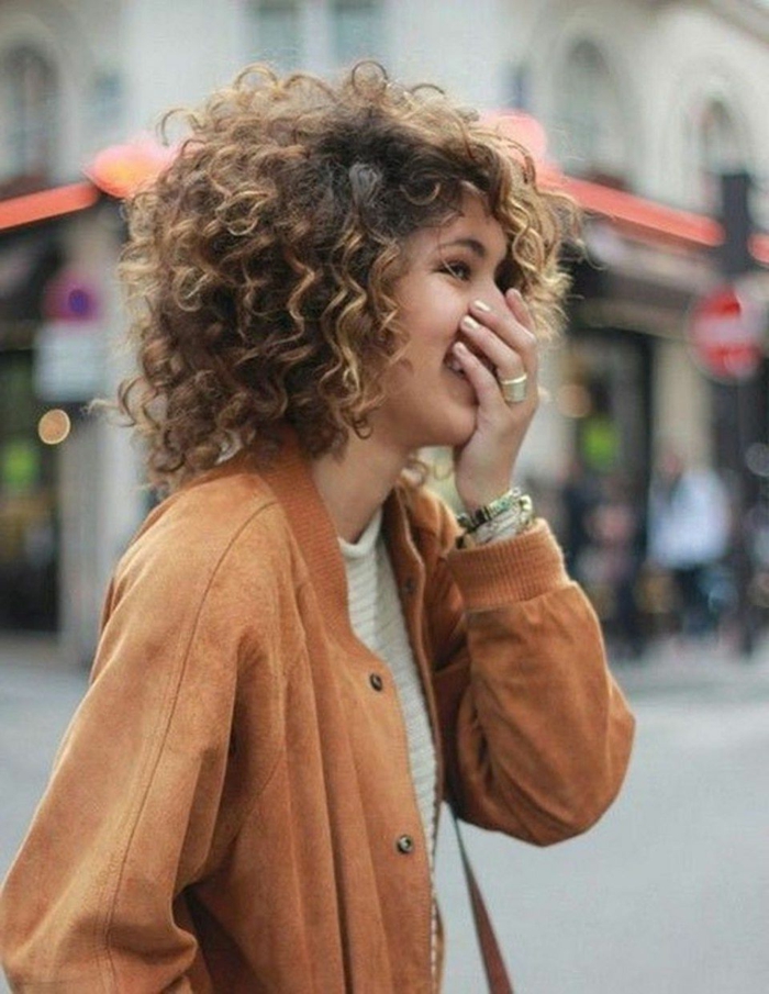 lachende junge dame casual street style braune jacke kurzhaarfrisuren mit locken dunkle haare mit blonden strähnen