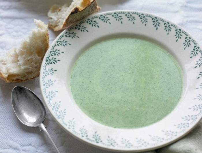 löffel aus metall brot ein weißer teller mit grüner suppe eine decke vegane suppe