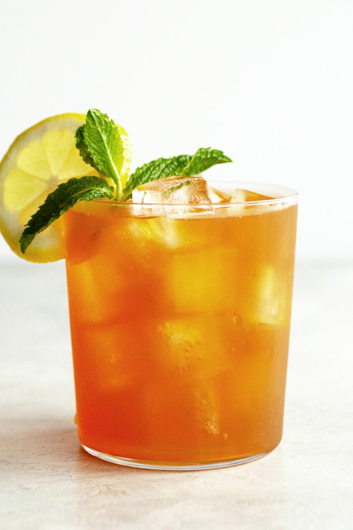 mango eistee selber machen rezept ein glas mit orangem getränk und eiswürfeln und pfefferminze und zitronen