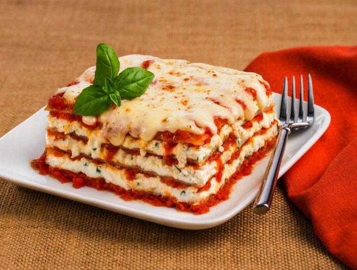 weißer teller mit lasagne bolognesse mit tomatensoße und bailikum eine gabel