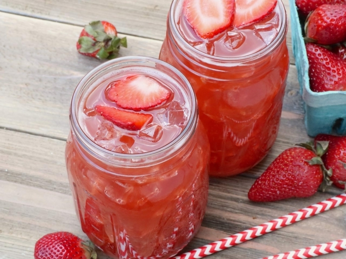 zwei lange rote strohhalme zwei gläser mit roten getränken mit eiswürfeln und geschnittenen erdbeeren