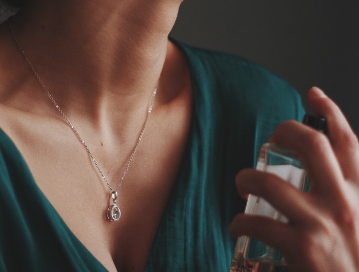 vertical shot of a female wearing a necklace with a diamond pendant spraying perfume on her