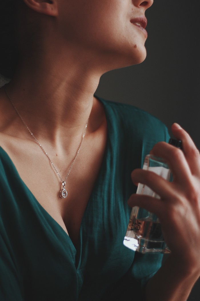 vertical shot of a female wearing a necklace with a diamond pendant spraying perfume on her