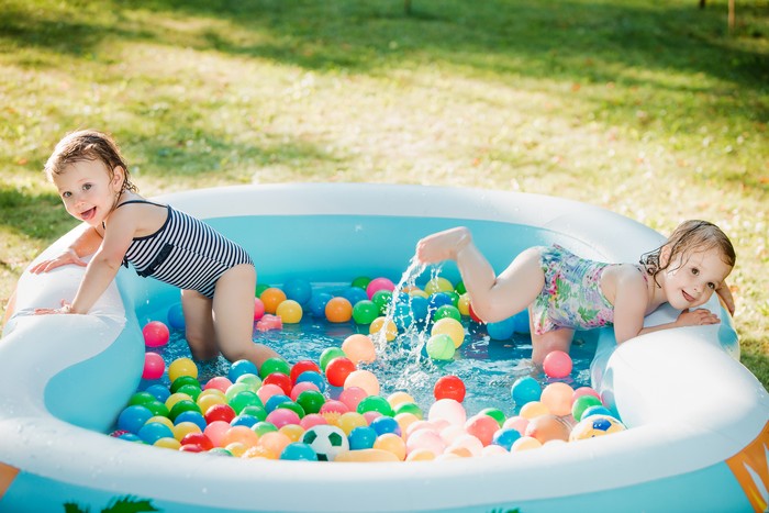 the two little baby girls playing with toys in inflatable pool in the summer sunny day