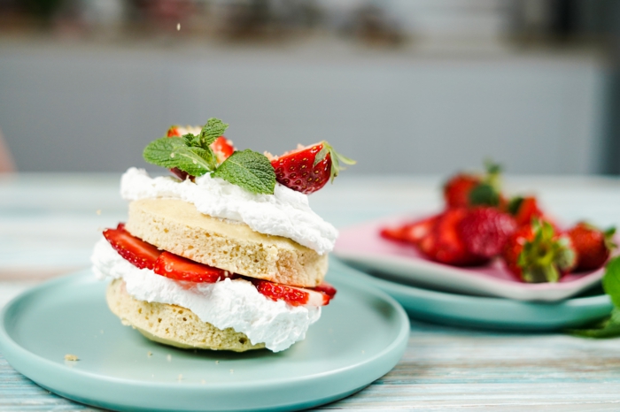 dekorative grüne blätter ein dessert mit erdbeeren und sahne zwei blaue teller mit strawberry shortcake