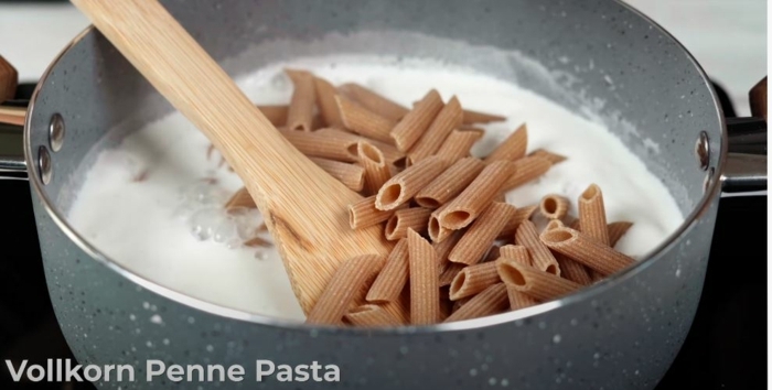 penne pasta in einer schüssel mit milch ein löffel aus holz