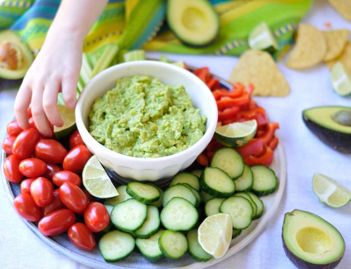 eine hand teller mit gemüse guacamole selber machen mit frischen tomaten avocado und knoblauch salate zum grillen