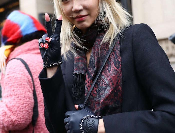 fashion week street style inspo schwarzer mantel chanel handschuhe bunter schal frau mit blonden haare macht friedenszeichen shag frisu mit pony