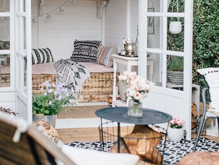 mini holz gartenhaus terrasse häuschen mit bett aus holz runder korbtisch schwarz weiß schwarzer teppich boho chic stil außeneinrichtung