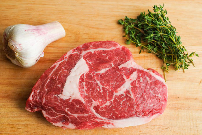 rib eye steak braten entrecote grillen rip eye steak zutaten frisches ribeye steak knoblauch grüne gewürze auf schneidebrett