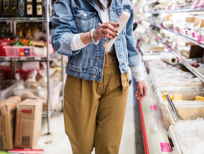 sportlich elegantes outfit weiße sneakers paperbag hose beige kombiniert mit blauer jeansjacke foto im supermarkt frau mit schwarzen haare