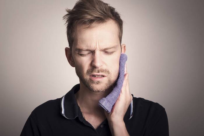 hausmittel zahnschmerzen zahnnerv beruhigen hausmittel entzündung im mund behandeln mann mit lila tuch am kiefer