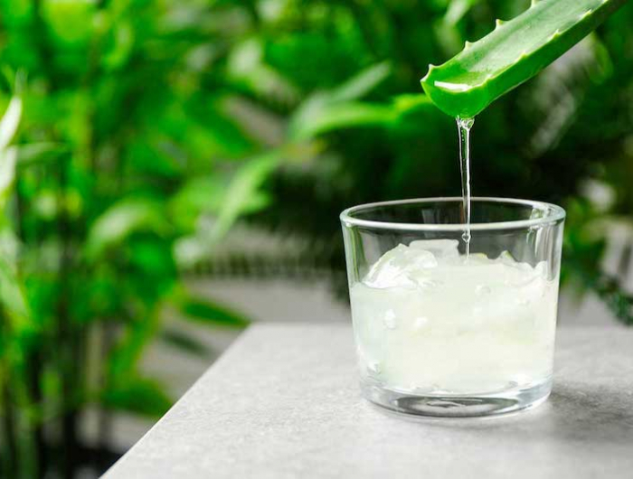 aloe vera juice dripping from leaf into glass on table against blurred background with space for tex