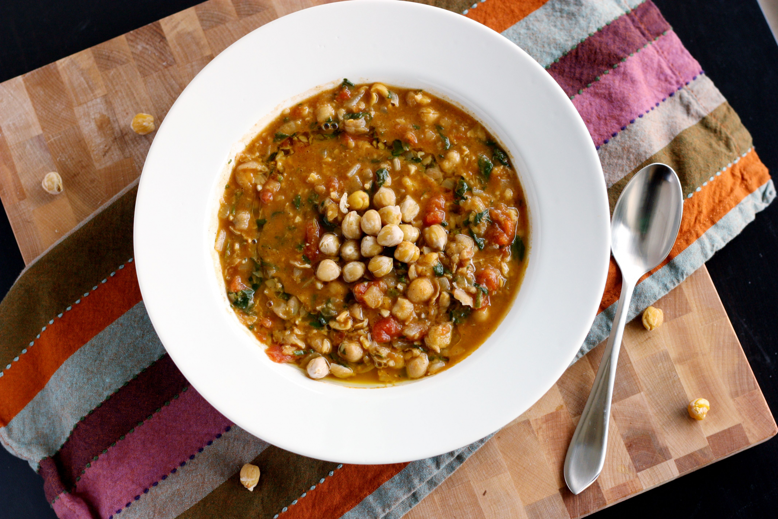 kichererbsensuppe mit spinat im weißer schüssel mit silberlöffel essen