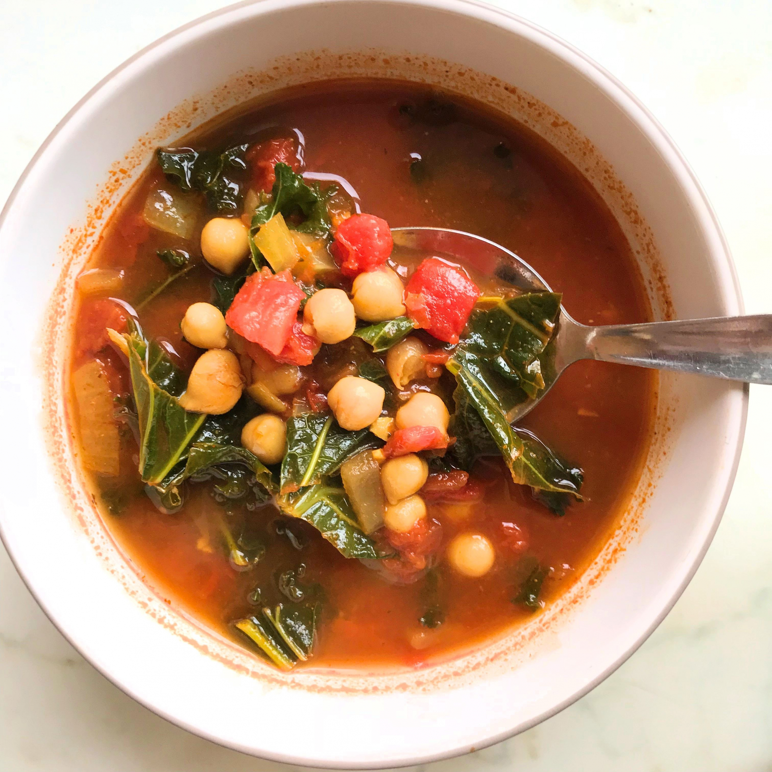 kichererbsensuppe mit spinat und tomaten in einer weißen schüssel