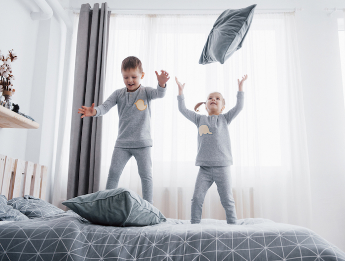 happy kids playing in white bedroom. little boy and girl, brother and sister play on the bed wearing pajamas. nightwear and bedding for baby and toddler. family at home