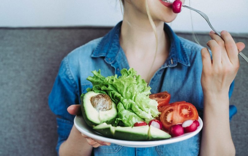 young woman eating fresh vegetables at home. vegan eating avocado, salad, radish and tomatos