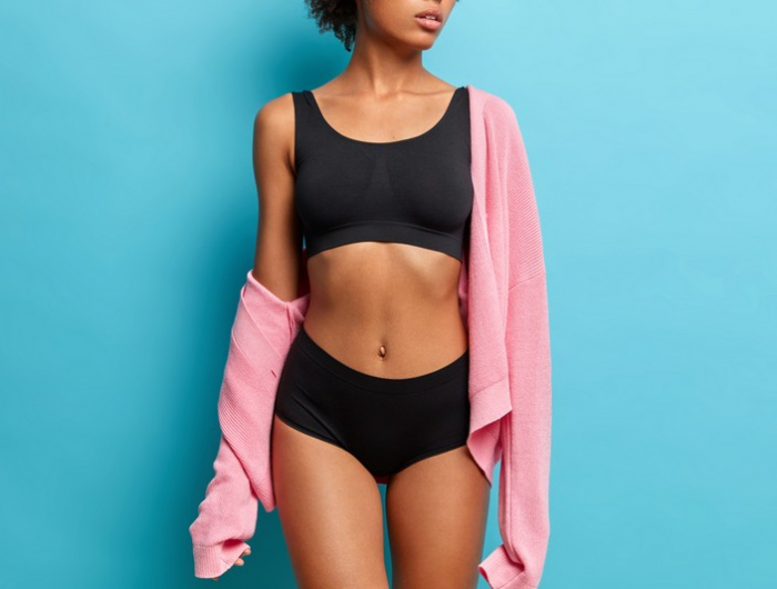 cropped image of sexy woman with perfect figure dressed in black underwear has flat abdomen isolated on blue background. sporty female body for your motivation