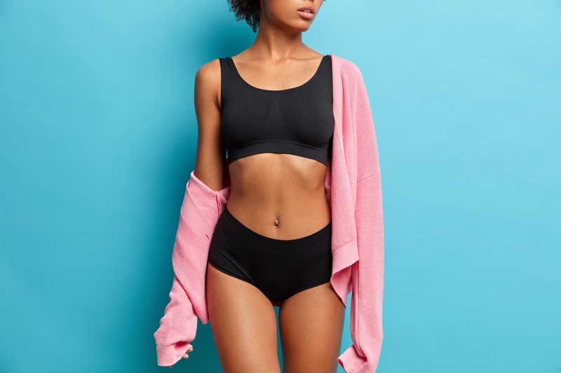cropped image of sexy woman with perfect figure dressed in black underwear has flat abdomen isolated on blue background. sporty female body for your motivation