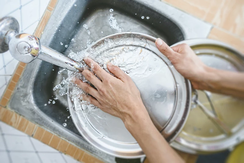 cropped hands of woman washing dishes in kitchen sink