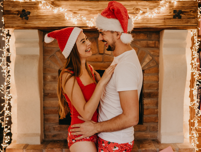 weihnachtsgeschenke zum selber machen geschenk eltern auswählen junge paar in roter unterwähsche weihnachtshut vor dem kamin