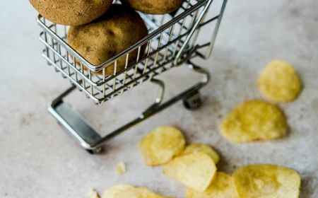 kartoffelchips, dahinter rohe kartoffeln in miniatur einkaufswagen