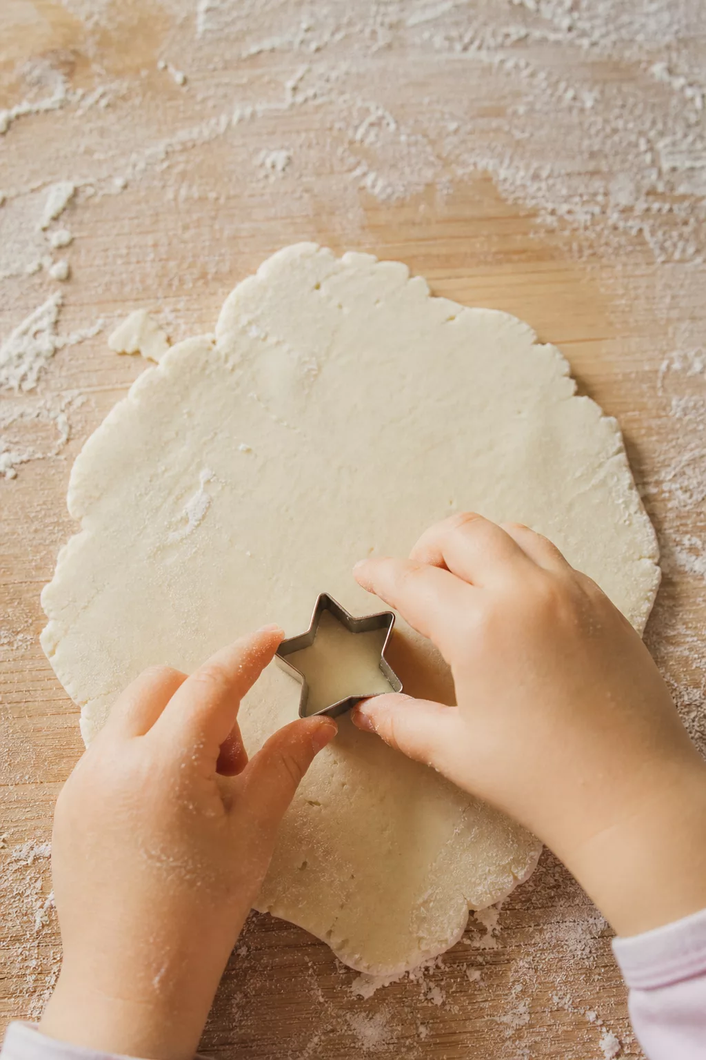 Kinderhände stechen Salzteig-Formen auf einem bemehlten Holzbrett aus